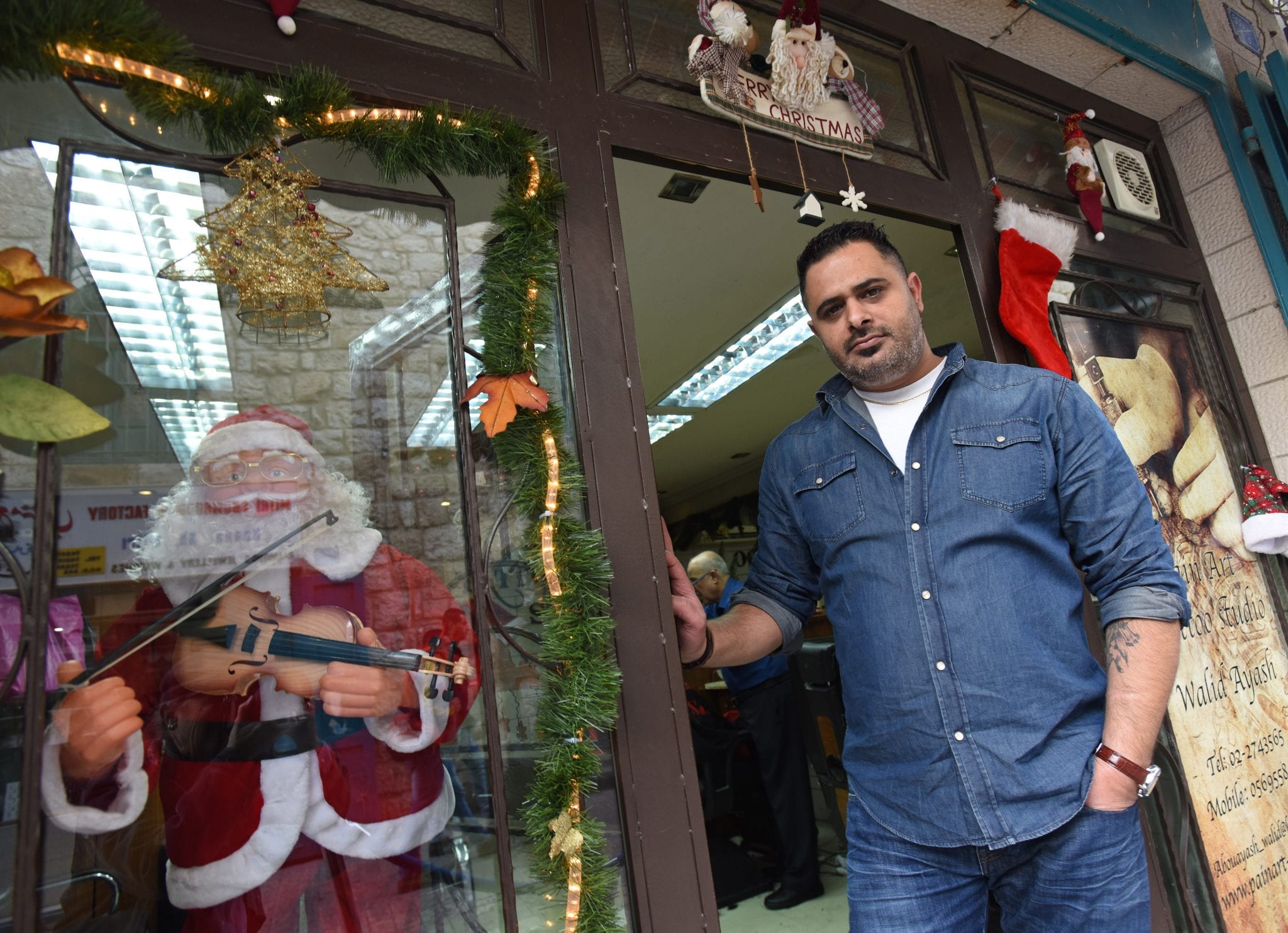 Palestinian Catholic Walid Abu Ayash, 39, tattoo artist, stands at the entrance to his barbershop/tattoo parlor on December 5 in Bethlehem, West Bank. (Credit: CNS photo/Debbie Hill.)
