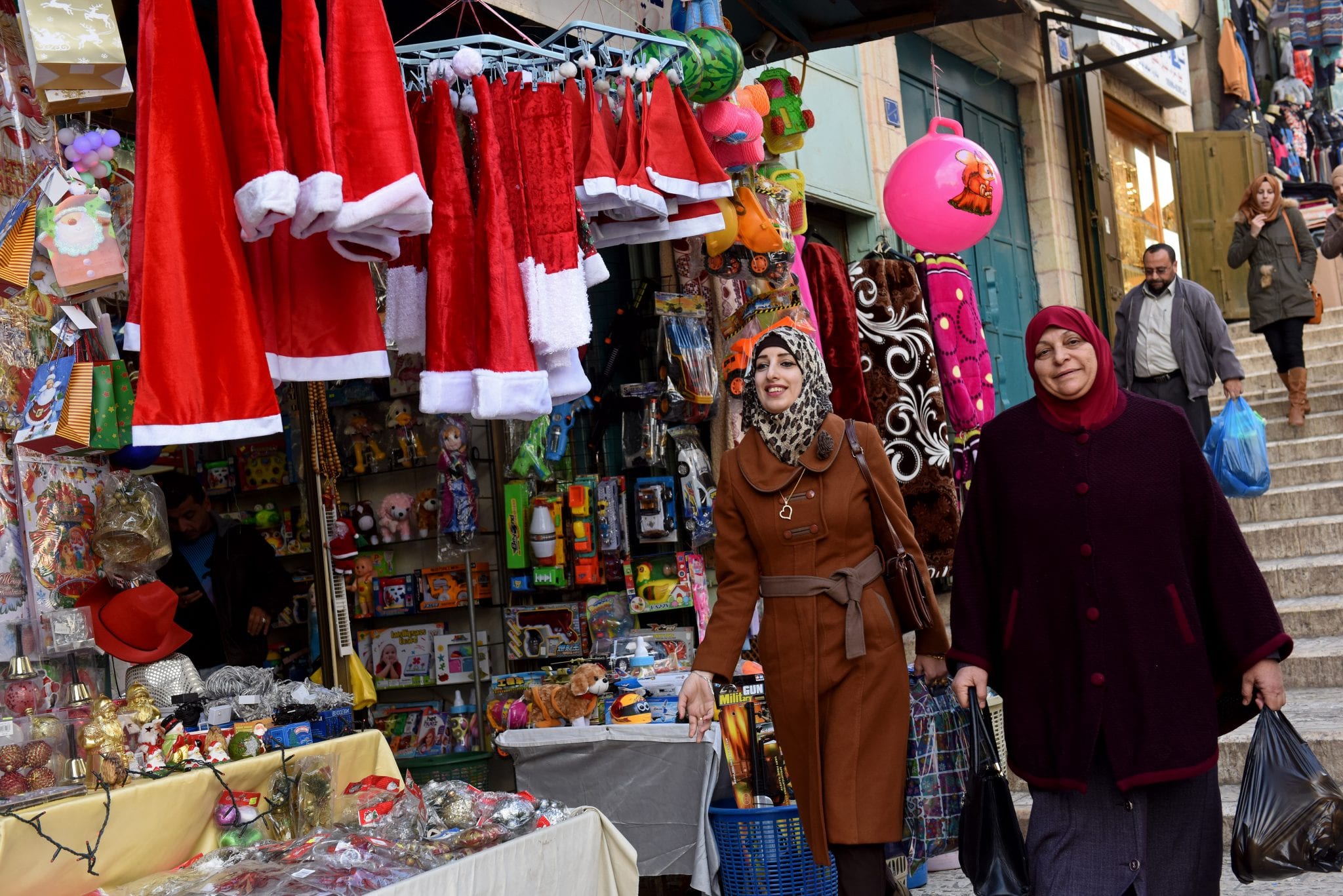 Palestinians walk past a shop selling Christmas decorations on December 5 near Manger Square in Bethlehem, West Bank. After two Christmas seasons in which the political reality had overtaken holiday cheer, people seem primed to finally feel some merriment in Bethlehem. (Credit: CNS photo/Debbie Hill.)