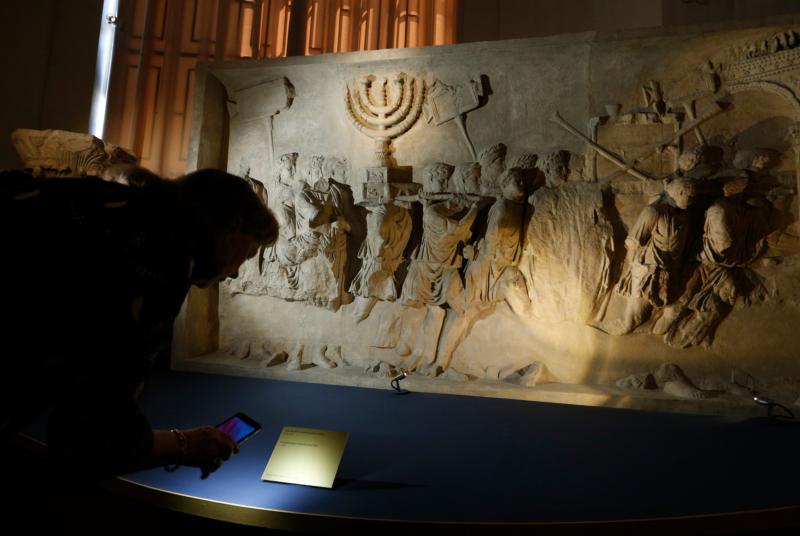 A journalist looks at a replica of the 1st-century Arch of Titus, showing Roman soldiers carrying the menorah, in a exhibition at the Vatican May 15. The replica is the central motif in a two-part exhibition on the menorah at the Vatican and at the Jewish Museum in Rome. (Credit: Paul Haring/CNS.)