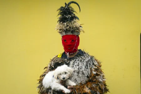 Parishioner Francisco Aguero dressed in a feather costume holds his dog as he poses for a picture, after attending a Mass celebrating Saint Francisco Solano, in Emboscada, Paraguay, Thursday, July 24, 2025. Hundreds of Catholic parishioners in Paraguay don bird-like costumes and parade down the streets to honor the 16th century saint said to possess miraculous powers. (Credit: Jorge Saenz/AP.)