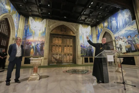 Artist Adam Cvijanovic, left, listens as Cardinal Timothy Dolan speaks during a media preview of the 25-foot-high mural, the largest artwork ever commissioned for St. Patrick’s Cathedral, in New York, Thursday, Sept. 18, 2025. (Credit: Richard Drew/AP.)