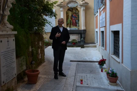 Mons. Peter Klasvogt, the rector of the Teutonic College poses for a photo next to the tomb of Burkhard Scheffler, a homeless man who died from the cold in 2022 on the edge of St. Peter's Square, and portrayed as St. Peter in a painting by German artist Michael Triegel, exposed in the chapel of the Teutonic College at the Vatican, Wednesday, Dec. 10, 2025. (Credit: Alessandra Tarantino/AP.)