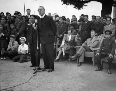Father Edward J. Flanagan, founder of Boy's Town, Nebraska, speaks into a microphone at Meiji Stadium in Tokyo, May 28, 1947 during a Japanese Boy Scout Jamboree. At right, wearing his school uniform, is Crown Prince Akahito. (Credit: Charles Gorry/AP.)