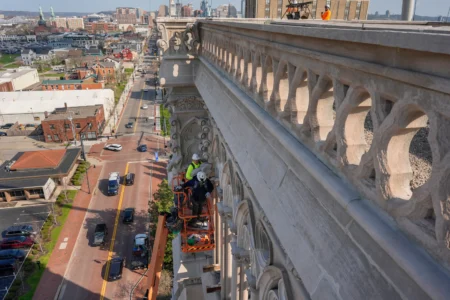 The final new terra cotta gargoyle is installed by Cole Burklund, in the bright yellow, and Blake Priest using a cherry picker high on the Cathedral Basilica of the Assumption, known as "America's Notre Dame," in Covington, Ky., on Monday, March 30, 2026. (Credit: Carolyn Kaster/AP.)