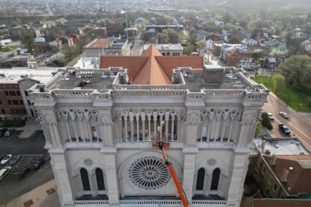 Workers are seen beyond an orange cherry picker high on the Cathedral Basilica of the Assumption, known as "America's Notre Dame," as the final new terra cotta gargoyle is secured with straps to the left, in Covington, Ky., on Tuesday, March 31, 2026. (Credit: Carolyn Kaster/AP.)