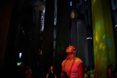 A visitor, bathed in sunlight streaming through the stained-glass windows, gazes up at the ceiling of the Sagrada Familia in Barcelona, Spain, Tuesday, May 26, 2026. (Credit: Emilio Morenatti/AP.)
