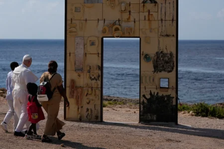 Pope Leo XIV walks together with a migrant family at the Gateway of Europe monument in Lampedusa, Sicily, southern Italy, Saturday, July 4, 2026, during a one-day pastoral visit to the island long associated with the plight of migrants crossing the Mediterranean. (Credit: Alessandra Tarantino/AP.)