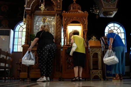 Pilgrims holding Fanouropites, orange-flavored cakes, kiss icons at the Church of St. Fanourios as an icon of Saint Fanourios, known in Greek as "The Revealer," is seen at left in Athens, Tuesday, Aug. 25, 2026. (Credit: Thanassis Stavrakis/AP.)
