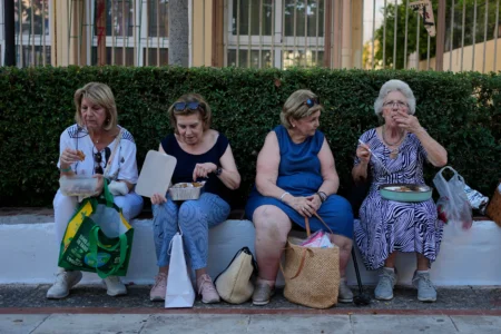 Pilgrims eat their Fanouropites, orange-flavored cakes, after a blessing at the Church of St. Fanourios in Athens, Wednesday, Aug. 26, 2026. (Credit: Thanassis Stavrakis/AP.)