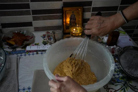 Maria Chanioti, 66, prepares Fanouropita, an orange-flavored cake, as a small icon of Saint Fanourios, known in Greek as "The Revealer," is seen in the background in Athens, Wednesday, Aug. 26, 2026. (Credit: Thanassis Stavrakis/AP.)