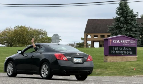 A driver waves while passing in front of Resurrection Lutheran Church and its church sign, featuring a seasonal pun, in Woodbury, Minn., on Sunday, Sept. 27, 2026. (Credit: Giovanna Dell'Orto/AP.)